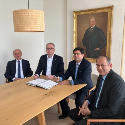 Auf dem Bild sind von links nach rechts Manfred Barfuss und Michael Hilmerich von HOPPECKE sowie Vivek Bhatia und Ketan Pendse von TKIL Industries. Alle vier Herren sitzen an einem Holztisch und unterzeichnen die Vereinbarung.
